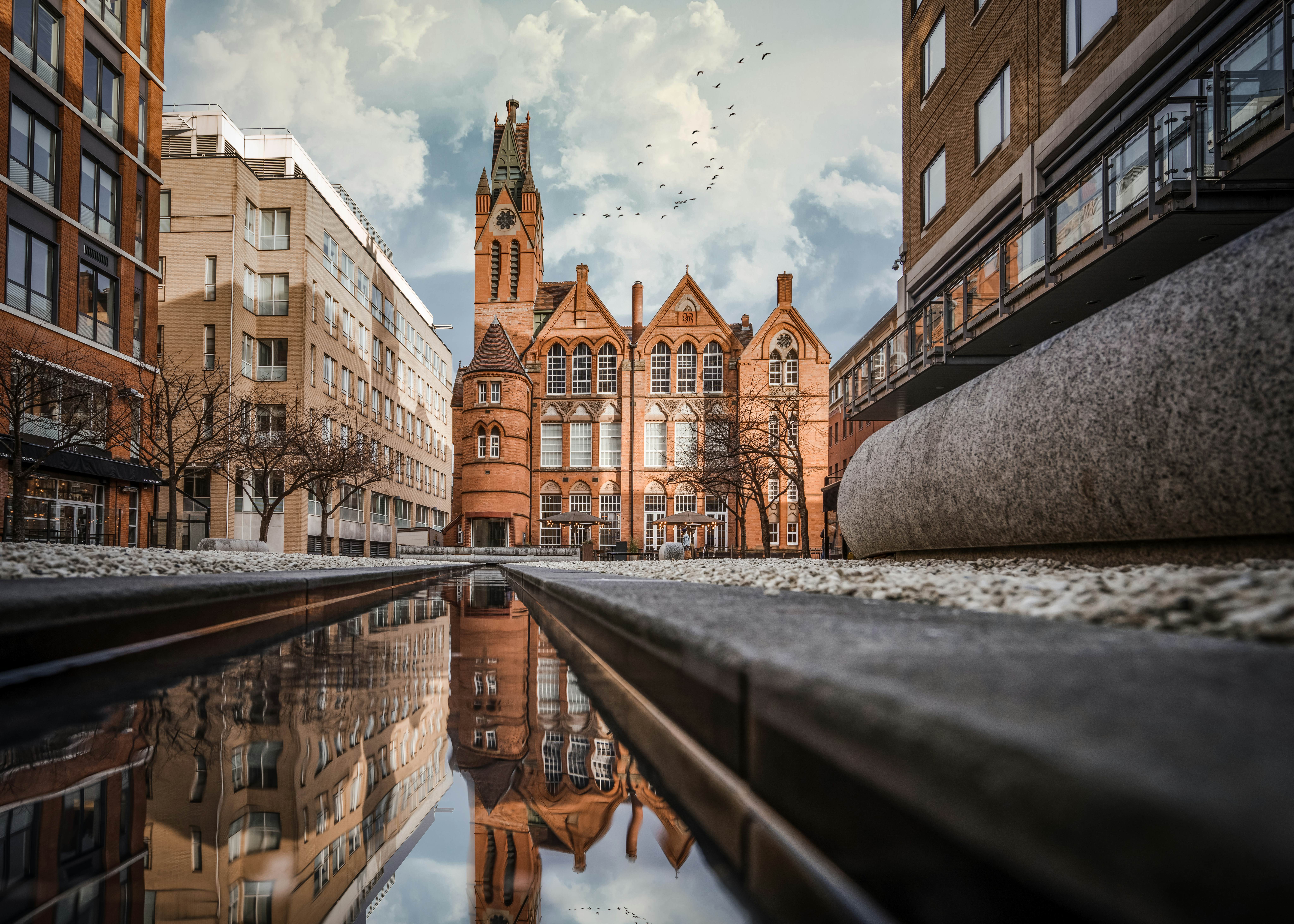 Brindley Place red brick church building reflected in water. West Midlands landmark buildings redevelopment in historic city centre reflection in stream. Birds and clouds in sky.